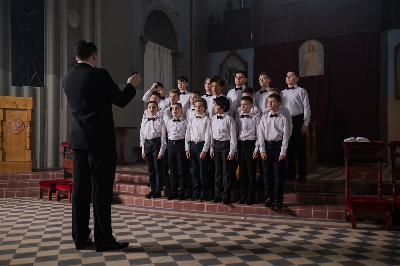 about-01 A boys choir performs under the guidance of a conductor in a formal indoor setting.